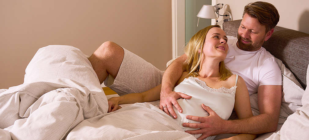 Schwangere Frau und Partner liegen auf dem Bett