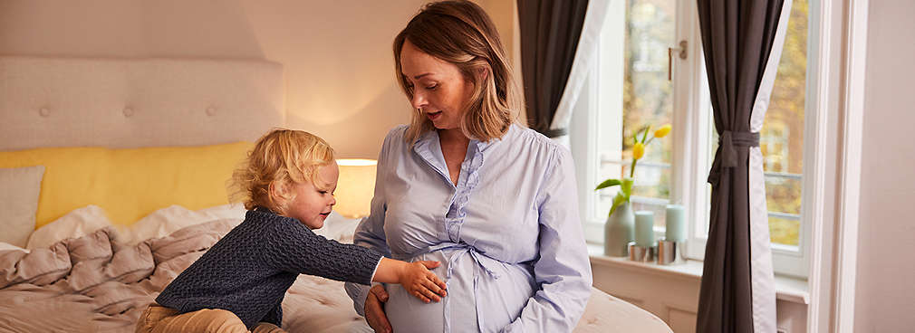 Schwangere sitzt mit Sohn auf dem Bett