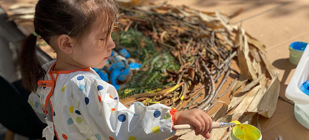 Kind bastelt einen Regenbogen aus Blättern, Ästen und Steinen