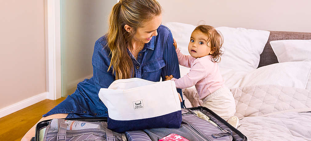 Mutter und Kind sitzen auf einem Bett und packen einen Koffer