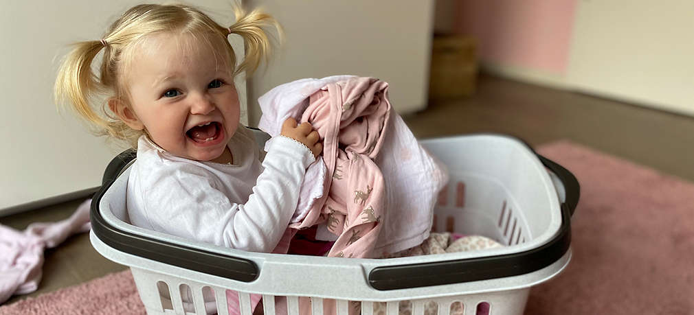 Kleines Mädchen sitzt im Waschkorb mit Wäsche in der Hand