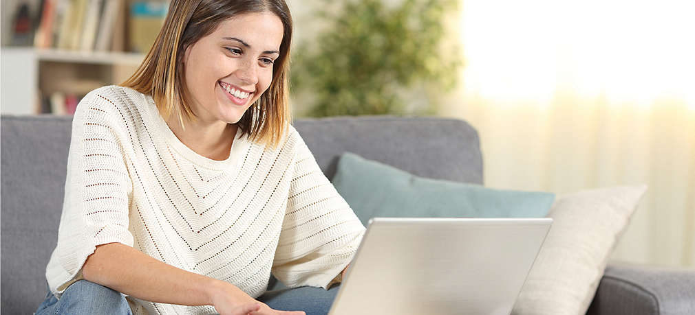 Frau sitzt auf der Couch und schaut in den Laptop