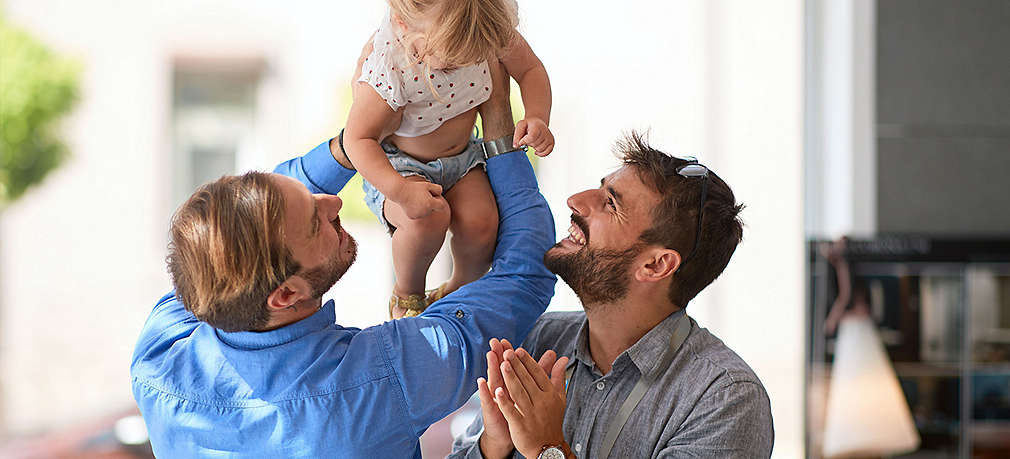 Zwei Väter lachen ihrem Kind zu