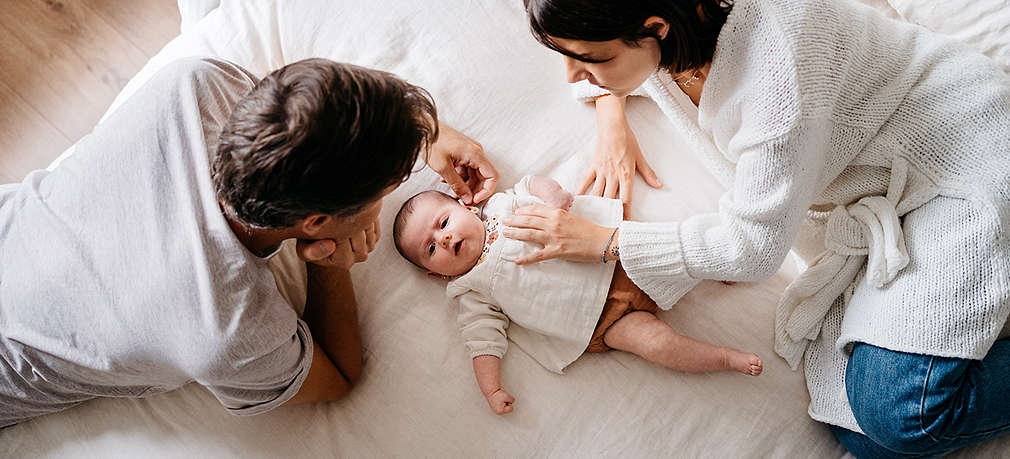 Mutter und Vater liegen mit Neugeborenem auf dem Bett