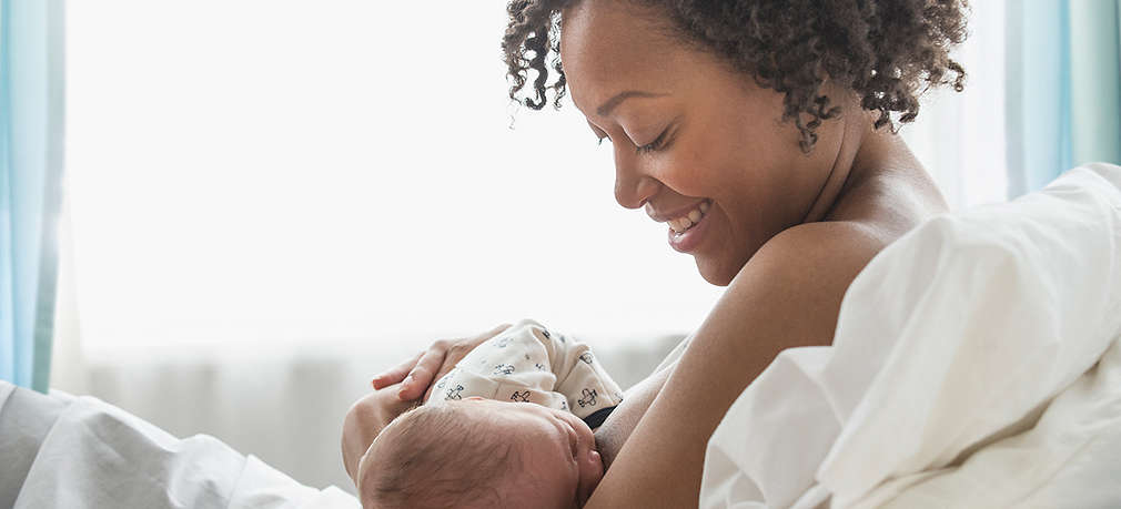 Frau stillt Baby im Krankenhausbett