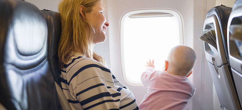 Baby sitzt im Flugzeug auf dem Schoß der Mutter und schaut aus dem Fenster