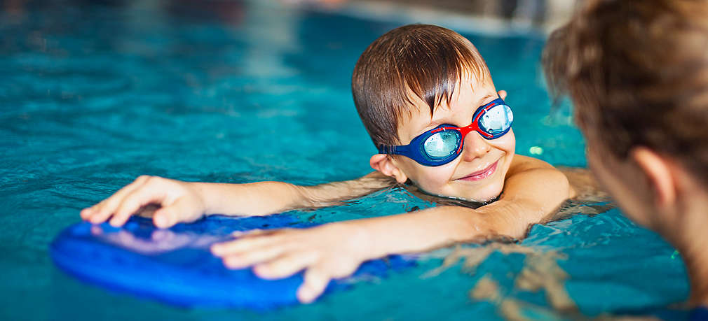 Frau hilft Jungen beim Schwimmen mit Schwimmbrett