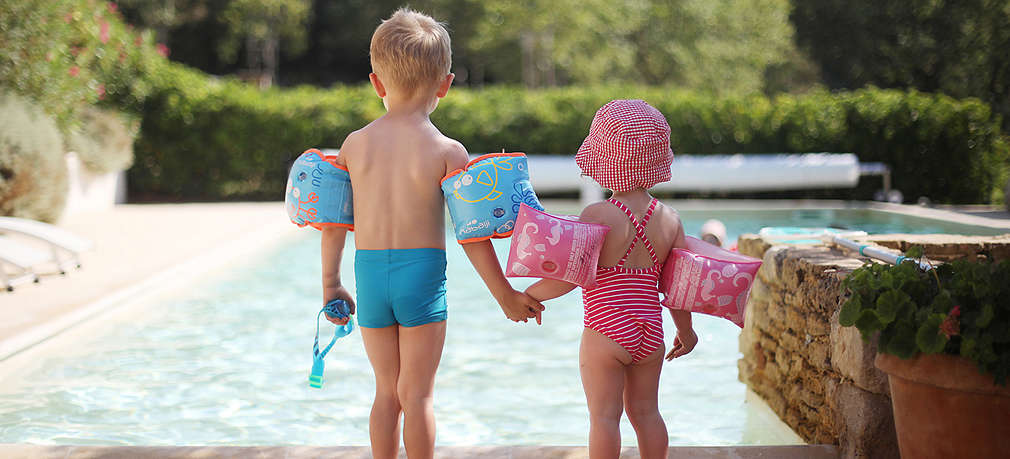 Ein Mädchen in rosaferbenem Badeanzug und ein Junge in blauer Badeshort stehen an einem Pool