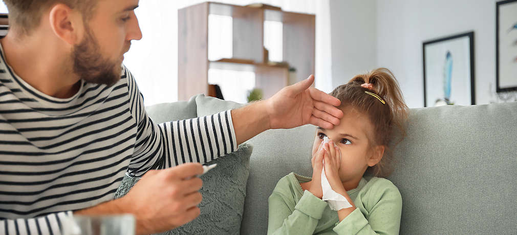 Mädchen putzt sich die Nase, Vater fühlt die Stirn