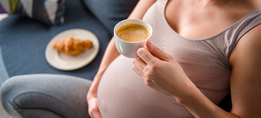 Schwangere Frau hält eine Tasse Kaffee in der Hand