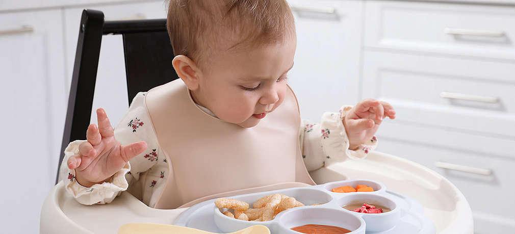 Baby sitzt im Hochstuhl und betrachtet seine Mahlzeit