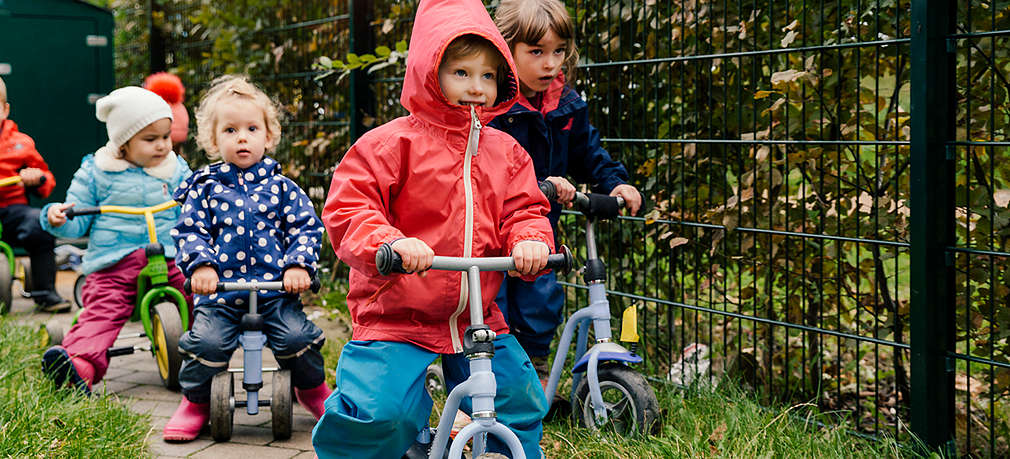 Kinder in Regenkleidung fahren auf einem schmalen Weg hintereinander Tretrad