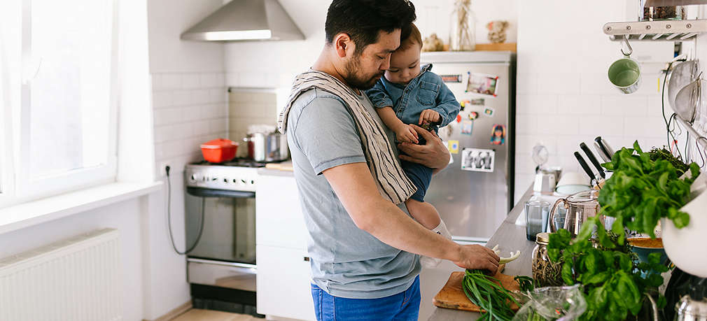 Vater kocht mit Kind auf dem Arm