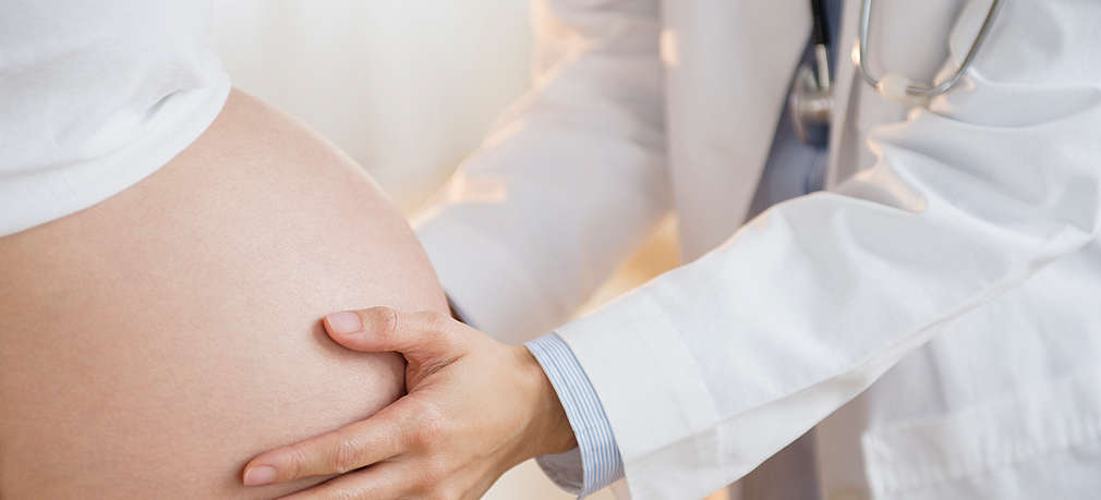 Arzt tastet Bauch einer schwangeren Frau ab 