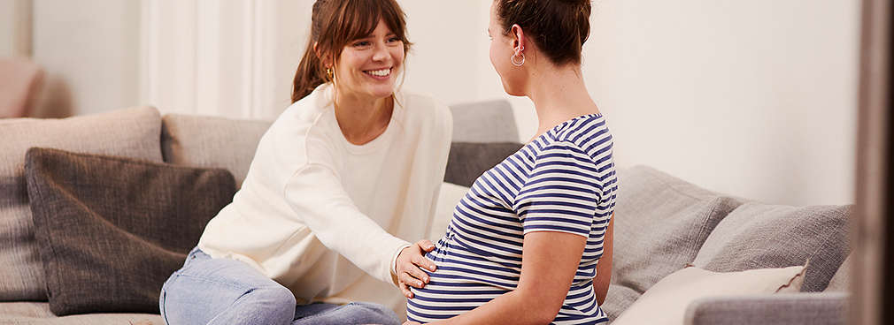 Frau legt Hand auf den Babybauch einer Freundin