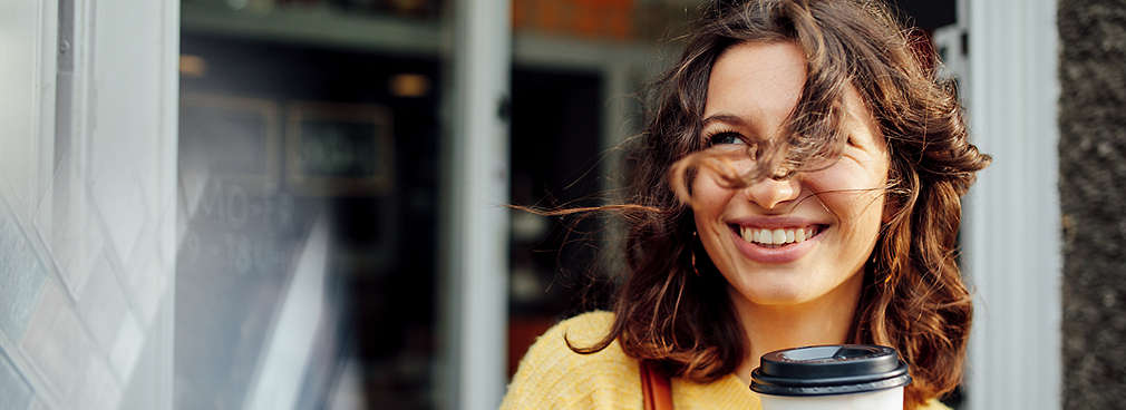Lächelnde junge Frau hält einen Kaffeebecher in der Hand und denkt über ihre berufliche Zukunft nach