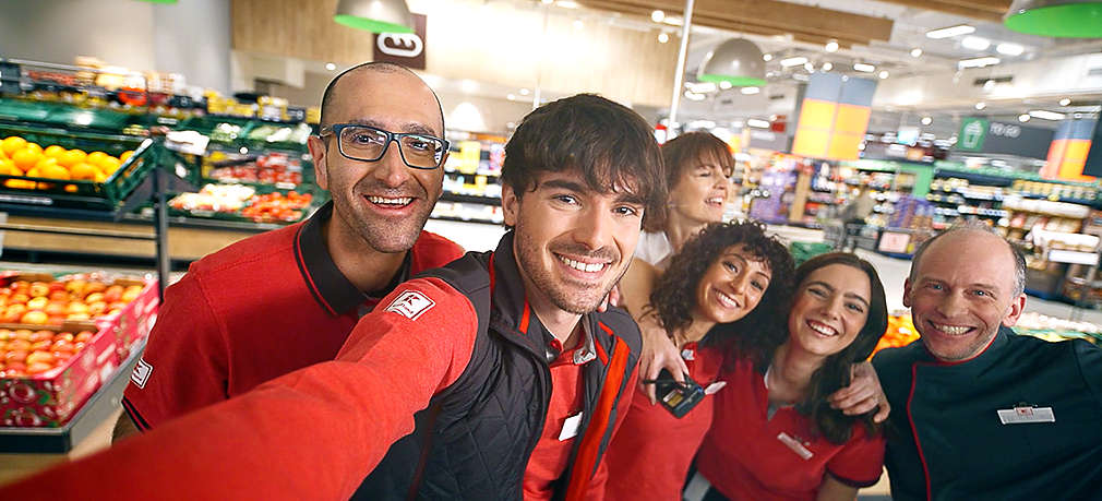 Kaufland-Mitarbeiter stehen im Markt und lächeln in Kamera
