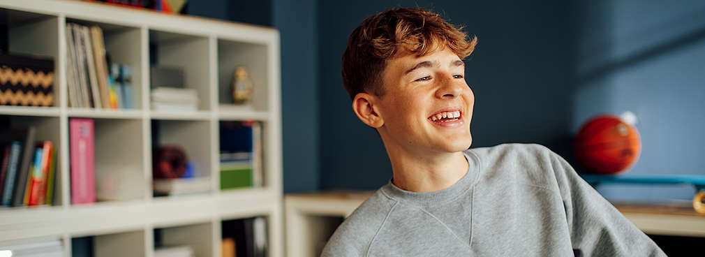 Lächelnder Junge denkt in seinem Jugendzimmer über ein Schülerpraktikum nach