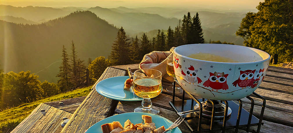 Mehrere Menschen in Tracht sitzen an einem mit Alpengerichten gedeckten Tisch