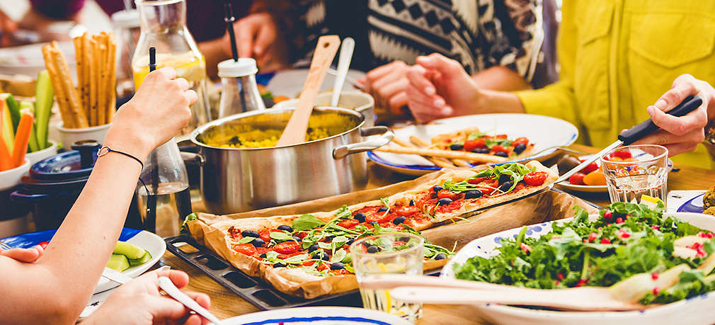 Vier Menschen im Anschnitt sitzen an einem gedeckten Tisch mit unterschiedlichen Gerichten und essen