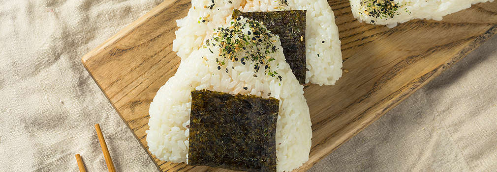 Zu sehen sind Onigiri, japanische Reisbällchen, auf einem Holzbrett