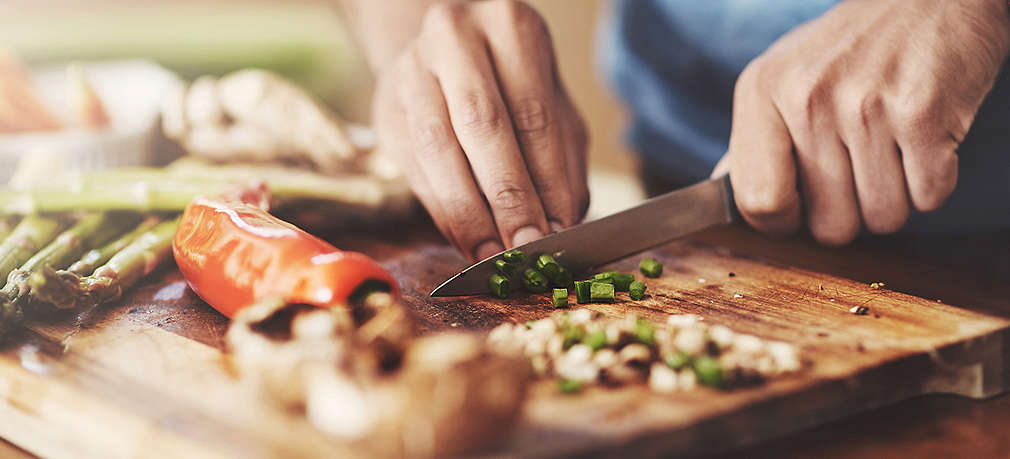 Koch schneidet Gemüse mit einem Küchenmesser auf einem Holzschneidebrett 