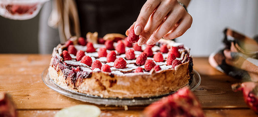 Mann dekoriert einen veganen Kuchen mit Beeren