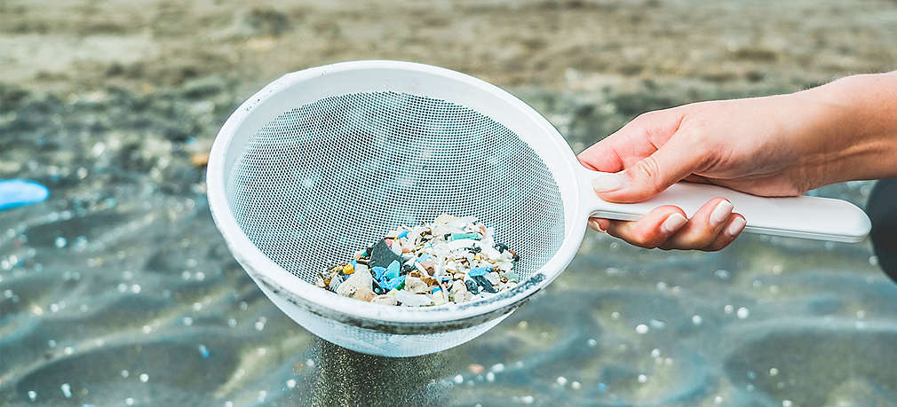 Hand hält Sieb mit Mikroplastikteilchen aus Gewässer