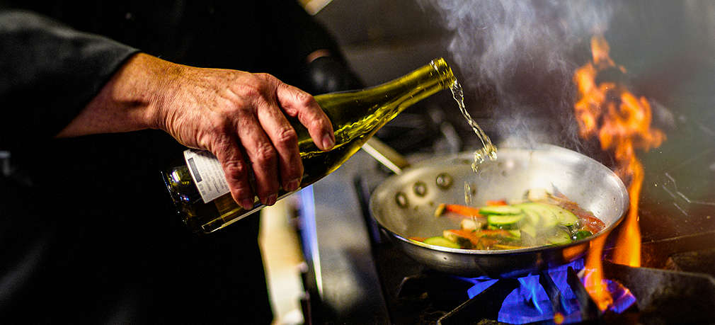 Koch löscht mit Wein das gebratene Gemüse in einer Bratpfanne ab