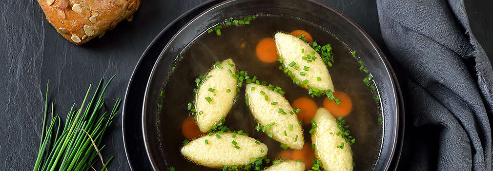 Suppe mit abgestochenen Nocken in einem schwarzen Teller, verfeinert mit Schnittlauch.