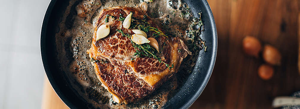 Steak wird mit frischen Kräutern und Knoblauch in einer Pfanne angebraten