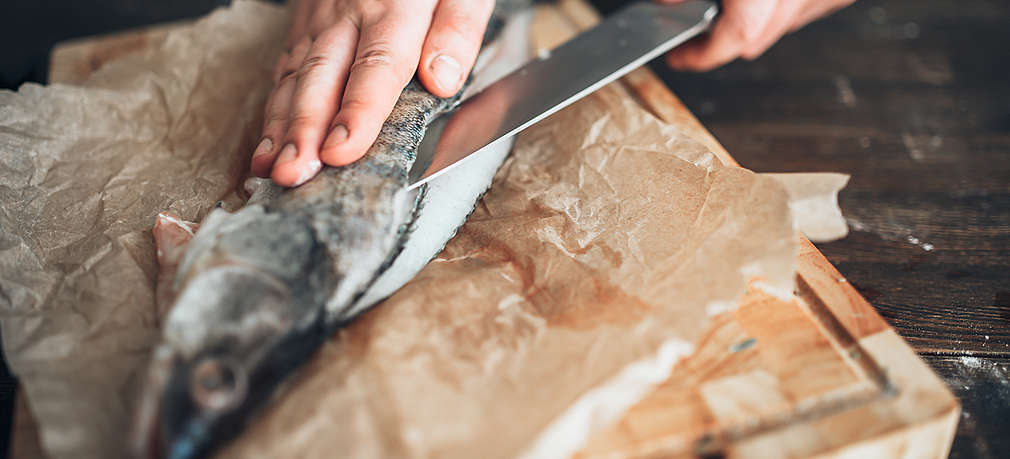 Ein Mensch filetiert eine Forelle mit einem Küchenmesser in der Hand
