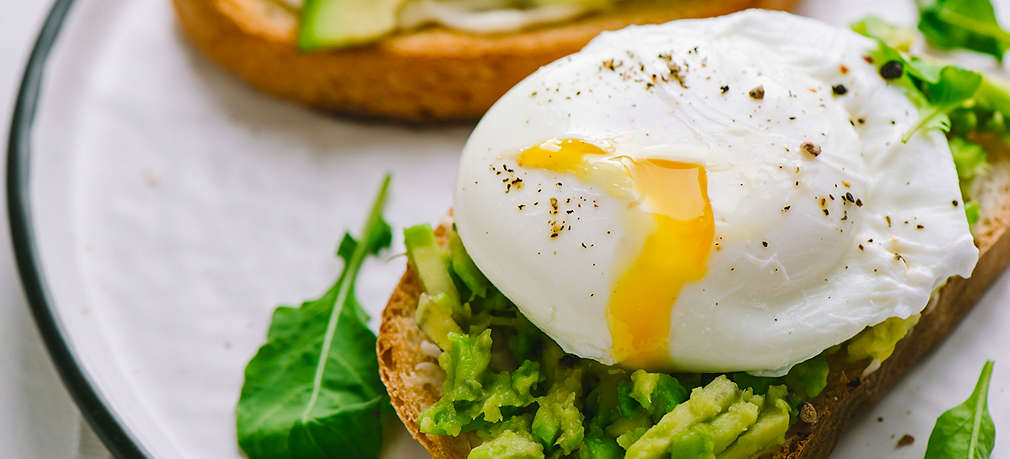 Ein Stück Brot belegt mit Salat und pochiertem Ei