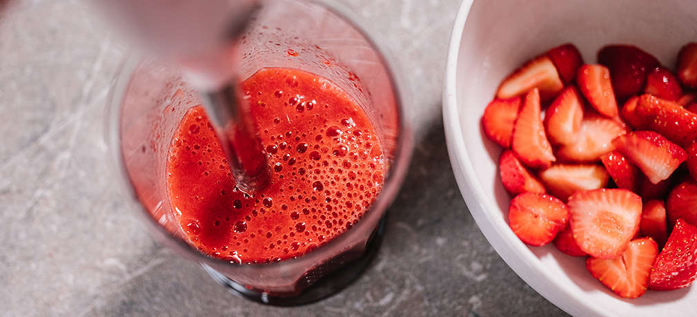 Kleingeschnittene Erdbeeren werden in einer Schale mit einem Handmixer püriert