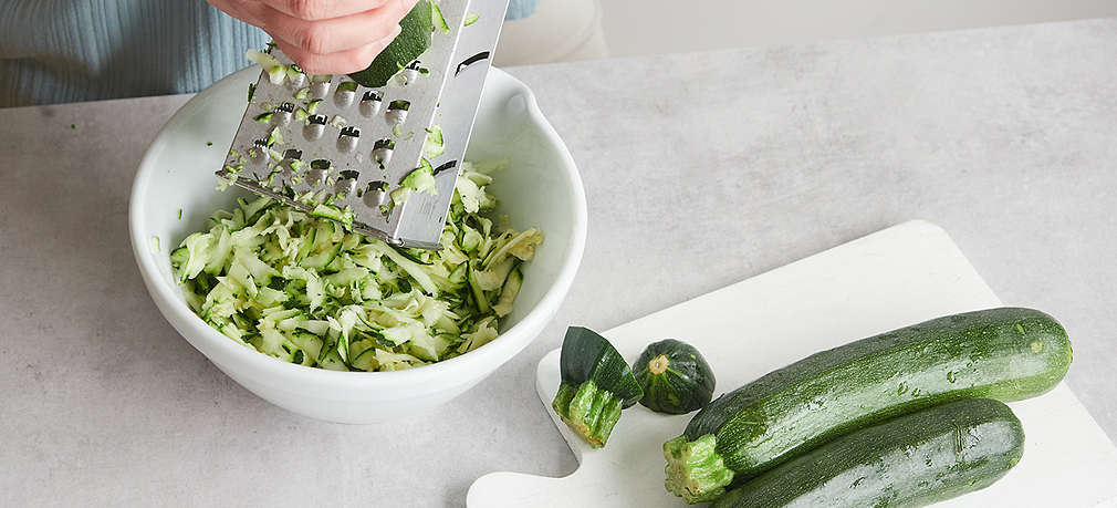 Frische Zucchini wird mit einer Handreibe grob gerieben