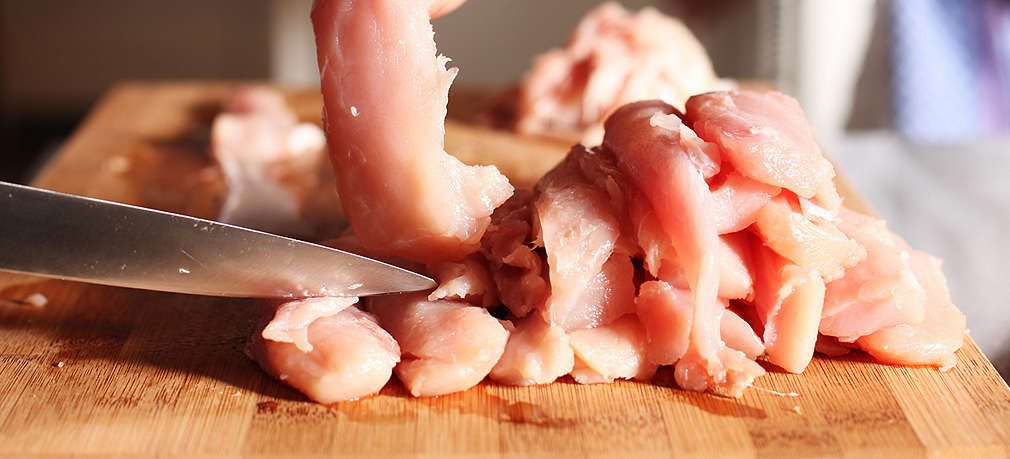 Hühnchenfleisch wird auf einem Holzschneidebrett in Streifen geschnitten