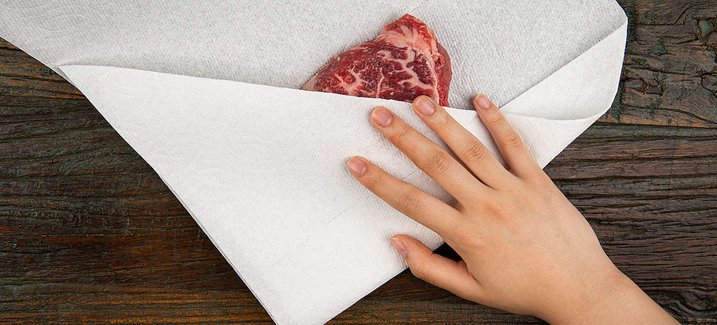 Ein Stück Fleisch wird mit Küchenpapier trocken getupft