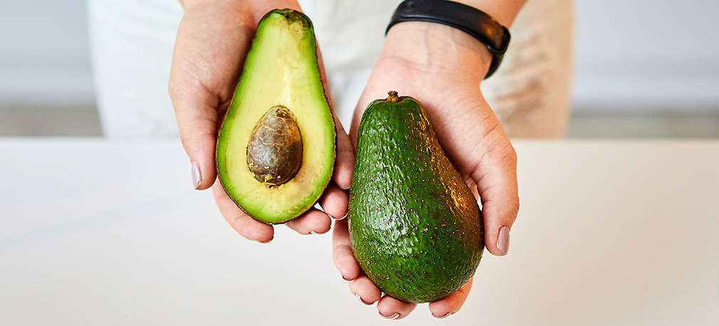 Zwei Hände im Anschnitt zeigen eine halbe und eine ganze Avocado