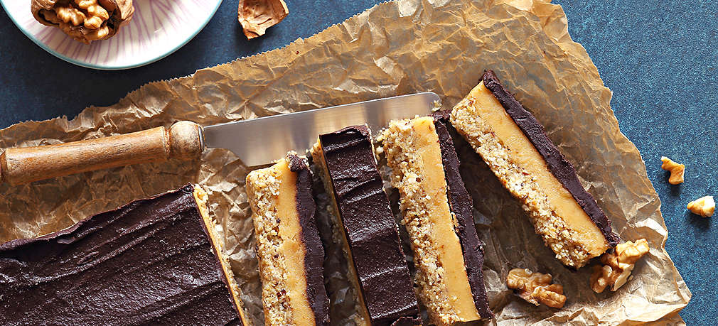 Selbstgemachter Kuchen ohne Mehl mit Keksboden, einer Creme und Schokolade auf Backpapier, daneben liegen ein paar Walnusshälften sowie ein Messer