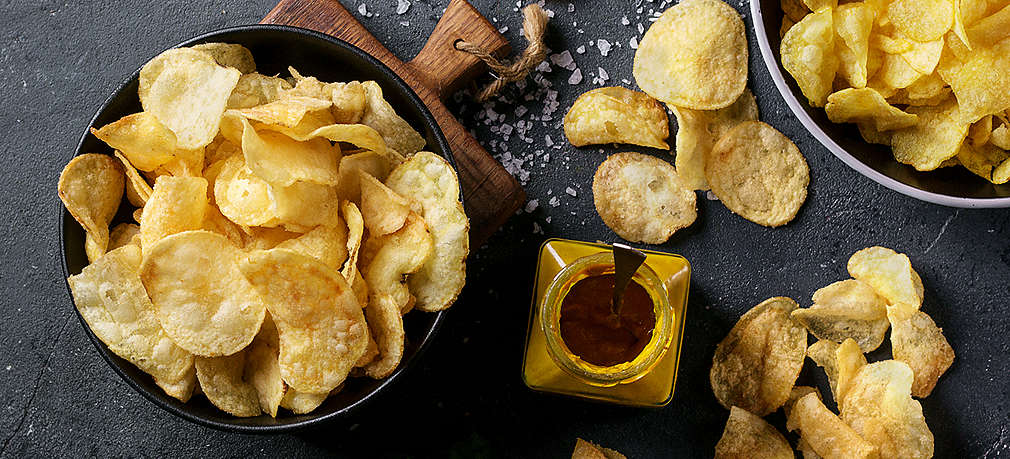 Selbstgemachte Kartoffelchips auf einem dunklen Grund sowie in zwei Schälchen