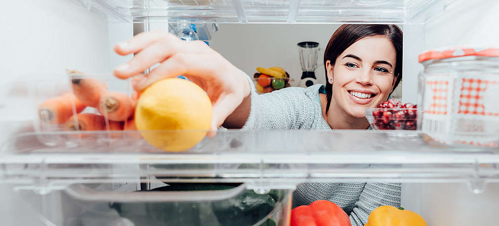 Frau greift im Kühlschrank nach Zitrone