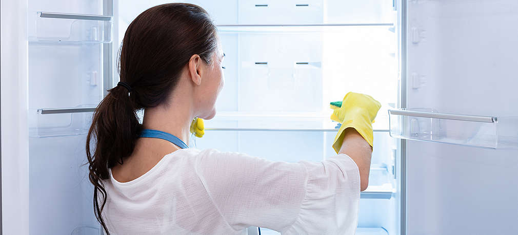 Frau reinigt den geöffnten Kühlschrank