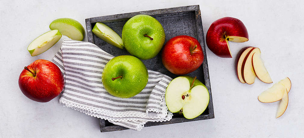 Mehrere rote und grüne Äpfel liegen auf einem grauen Tablet