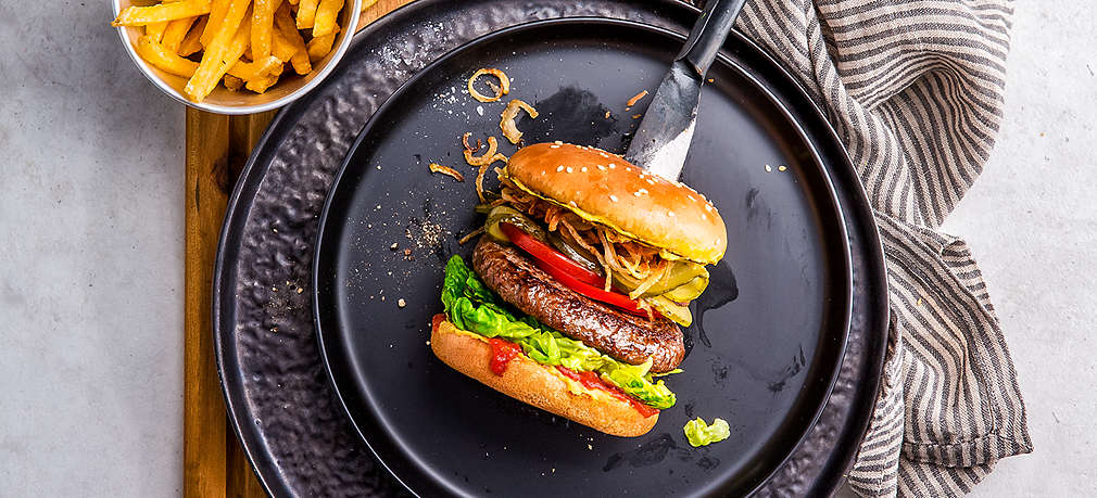 Burger von oben auf einem schwarzen Teller fotografiert, daneben eine kleine Schale mit Pommes