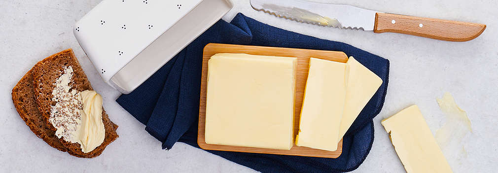 Ein Stück angeschnittene Butter in einer weißen Butterbox, daneben ein Buttermesser