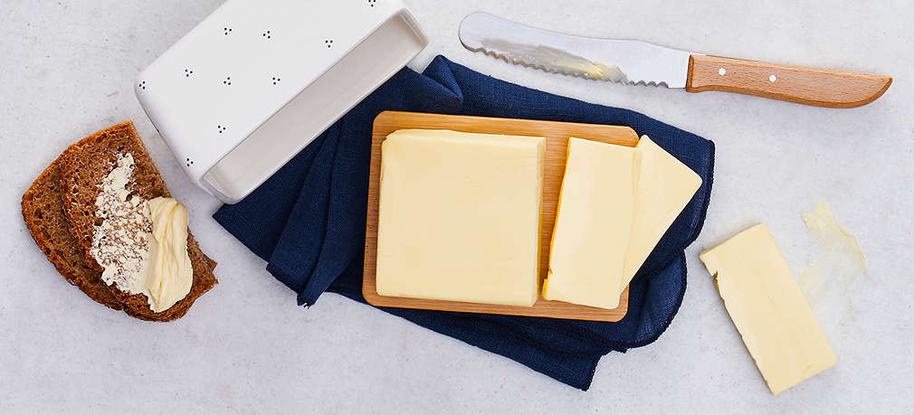 Ein Stück angeschnittene Butter in einer weißen Butterbox, daneben ein Buttermesser