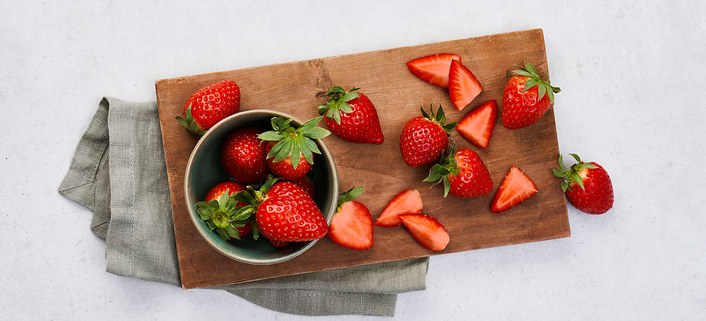 Mehrere Erdbeeren liegen angeschnitten oder im Ganzen auf einem Schneidebrett und in einer Schale
