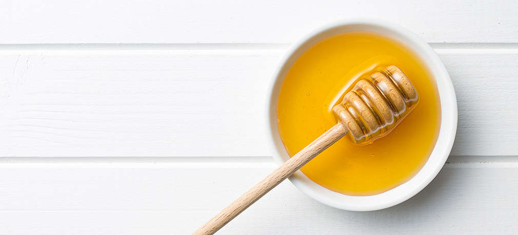 Flüssiger Honig in einem weißen Schälchen mit Honiglöffel aus Holz