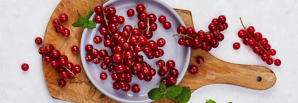 Eine graue Schale mit roten Johannisbeeren steht auf einem Holzbrett