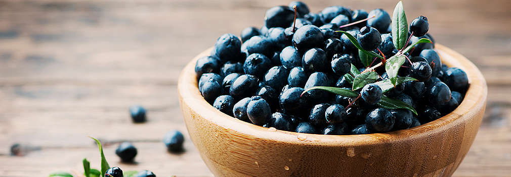 Myrtebeeren in einer Holzschale auf einem Holstisch, daneben ein frischer Myrtezweig mit Beeren und Blättern daran